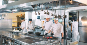 Five Chefs Wearing Uniforms Posing in a Commercial Kitchen