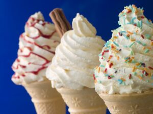 Whipped Ice Cream Cones with Three Different Toppings in a Row with Blue Background